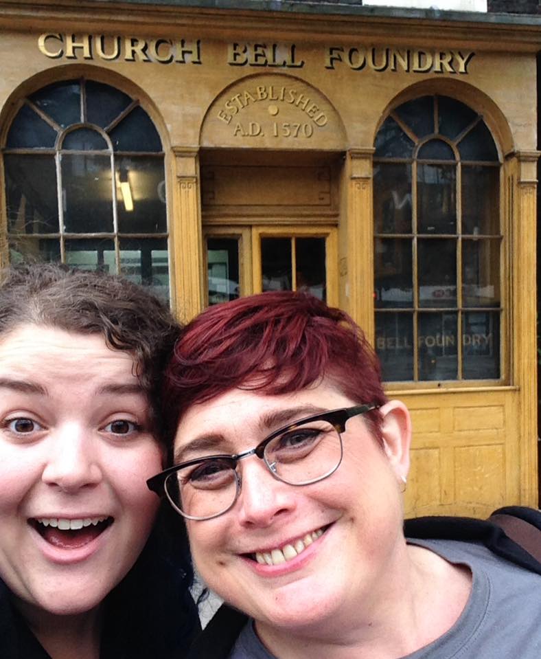 Val and Mel are smiling to the camera in front of the Whitechapel Bell Foundry storefront.